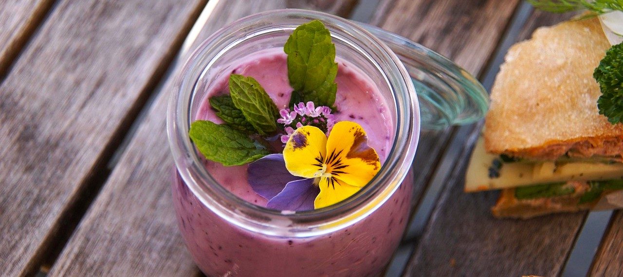 Lasinen jälkiruokakulho, jossa marjarahkaa ja koristeena orvokki.